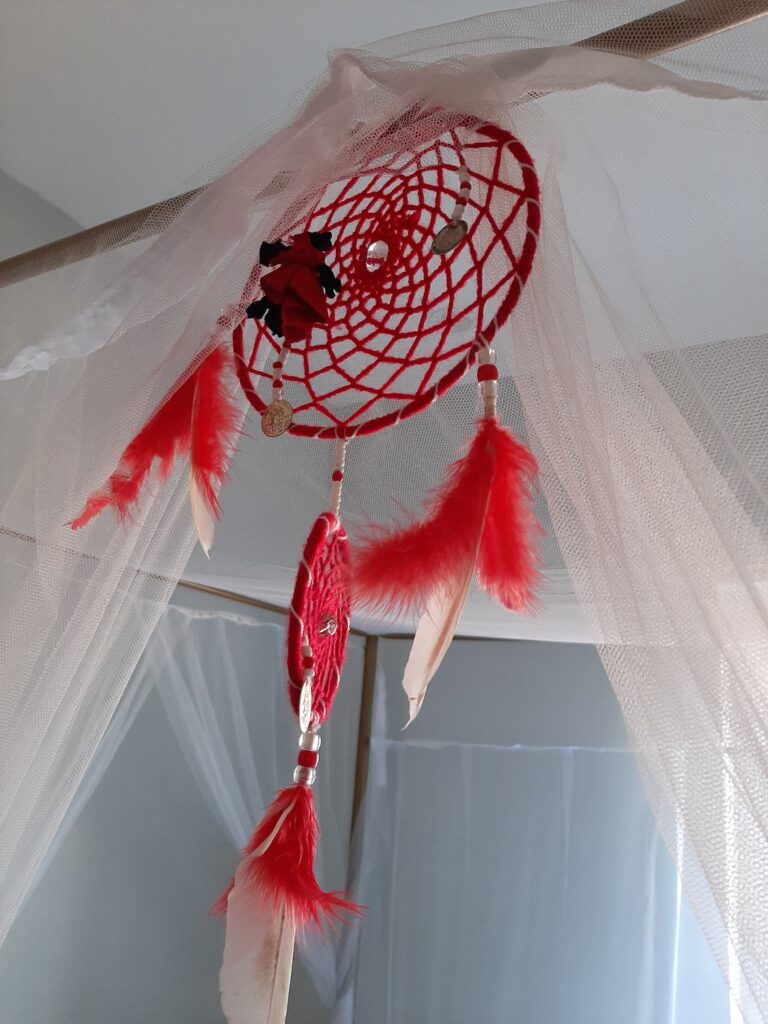 Photograph of a red crafted "dream catcher" with feathers.