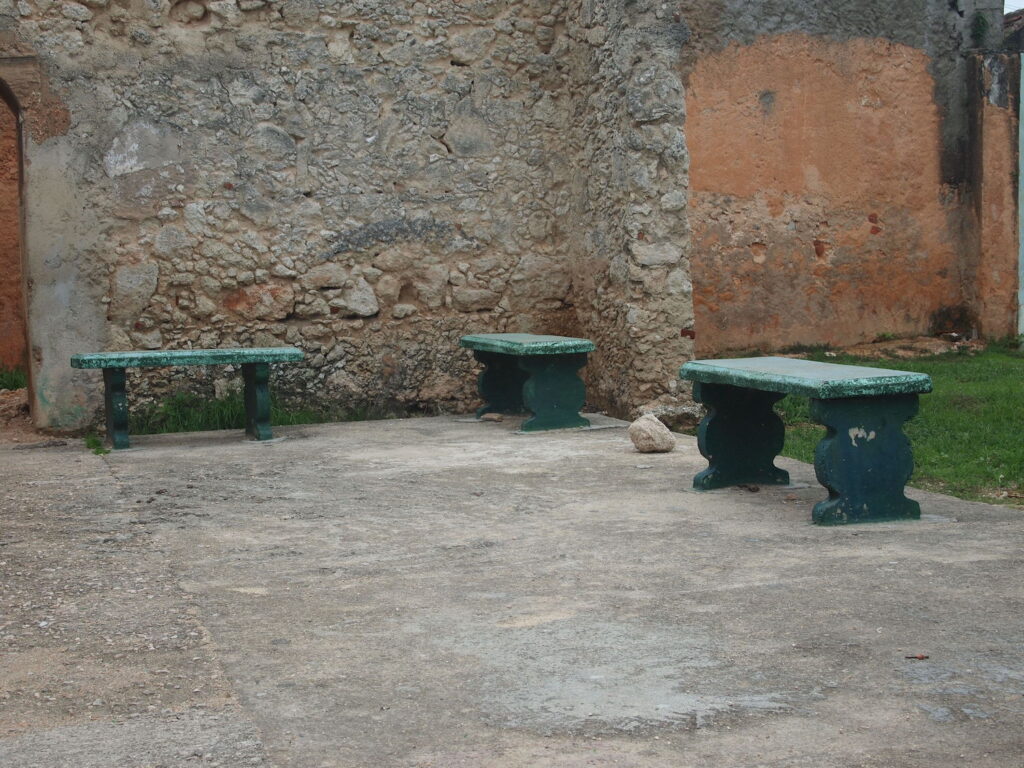 Photograph of three green concrete benches in front of a exposed concrete wall.