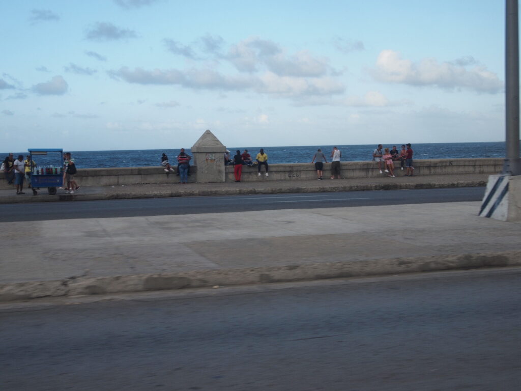 Photograph of people sitting on a concrete barrier by the ocean.