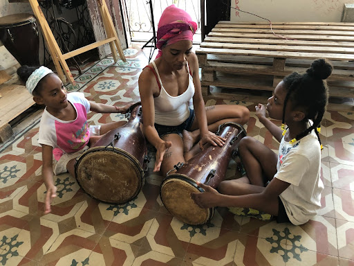 Photograph of Siria teaching bata drums to two children.