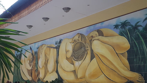 Photograph of a wall mural of women, musical instruments, and tropical foilage.