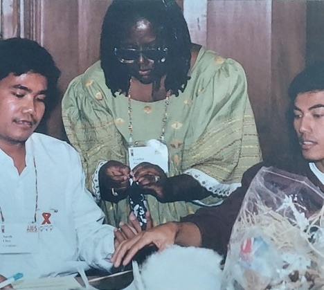 Davis, wearing a green and yellow dress and sunglasses, leans over two workshop participants with cloth in her hands