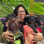 Tanya holding five large, Black dolls made of cloth and dressed in colorful fabrics