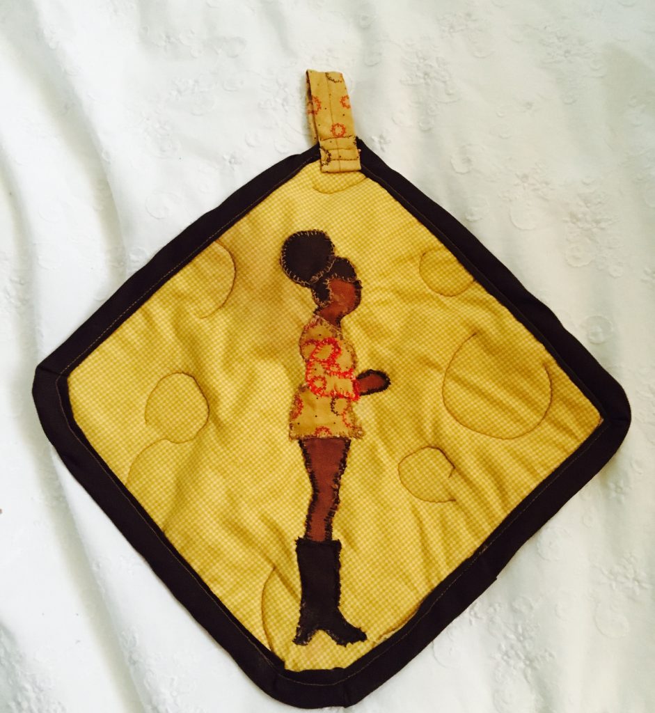 Potholder amarillo tejido que representa a una mujer Negra con un puff afro, vestido amarillo y botas negras altas