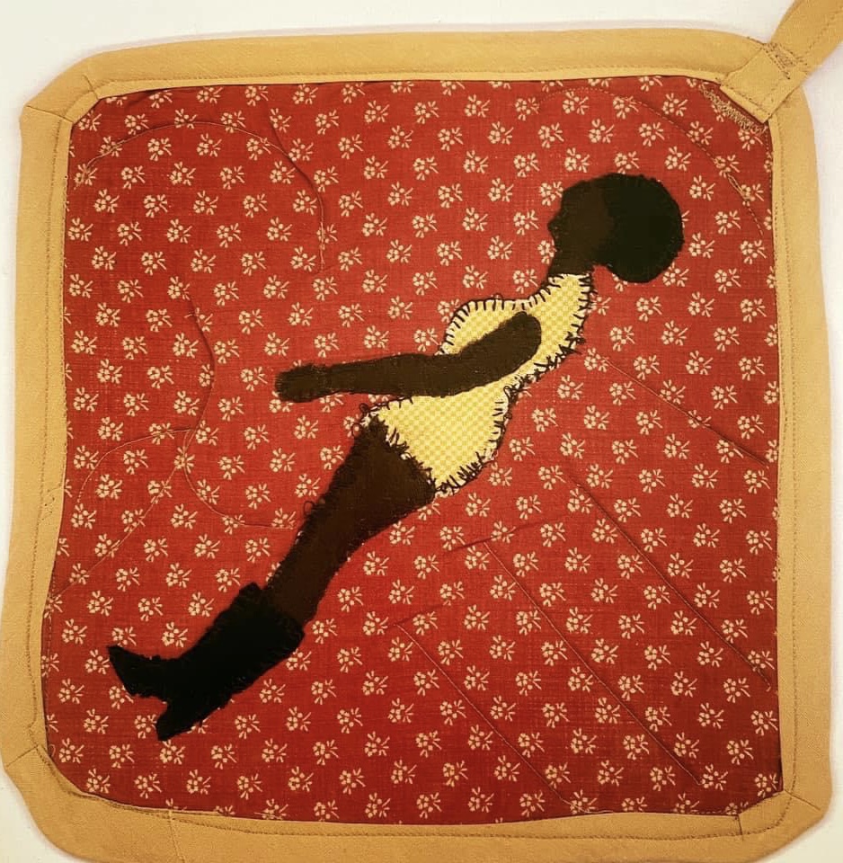 Potholder rojo tejido con ribete amarillo que representa a una mujer Negra con un vestido amarillo, un afro y botas negras altas