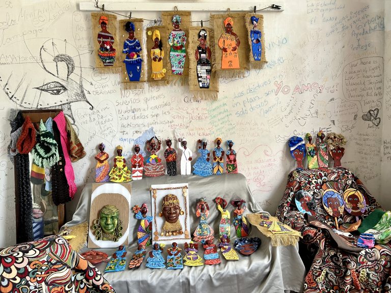 Various Black dolls and pieces of artwork featuring Black women dressed in vibrant colors displayed on a table and wall