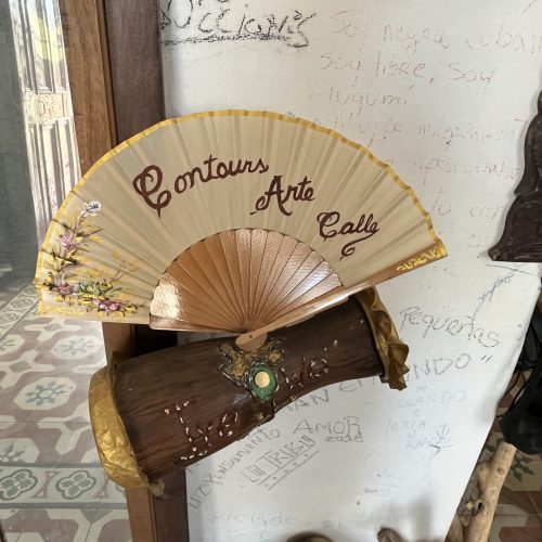 Golden fan posed on a drum, inscribed with the words "Contours Arte Calle" and painted flowers